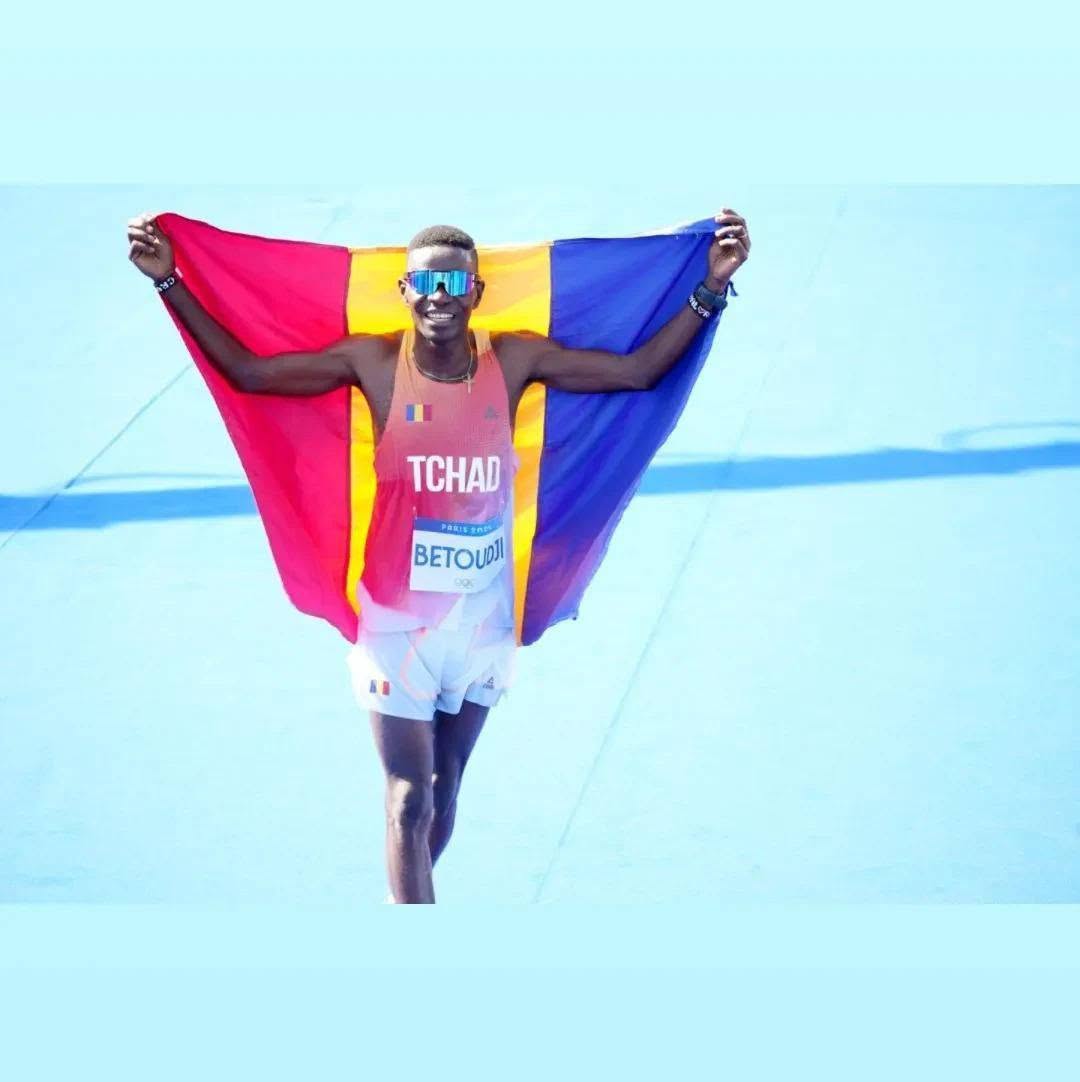 Valentin Betoudji franchissant la ligne d'arrivée du marathon de Paris 2024, drapeau du Tchad déployé